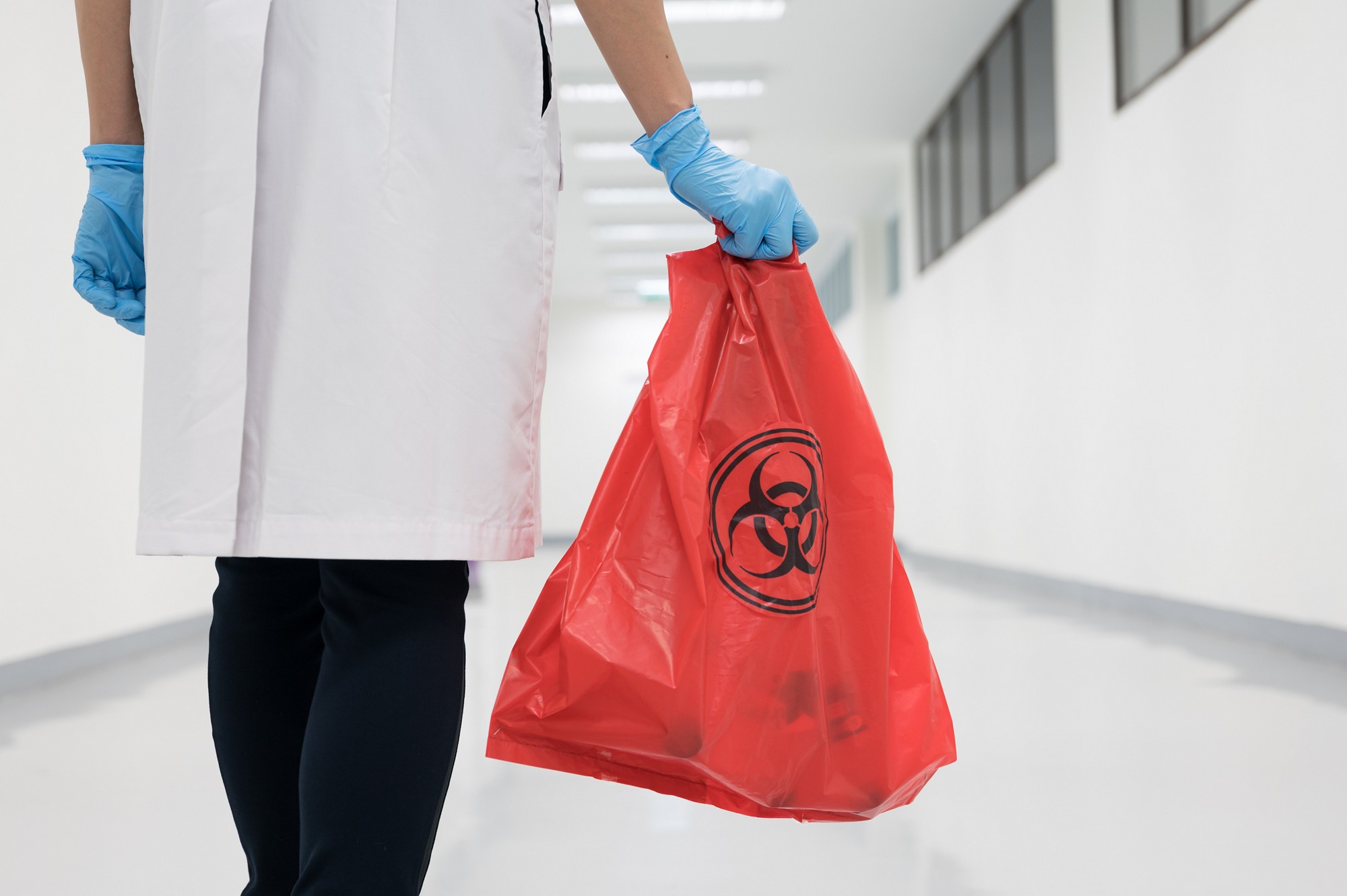 Scientist wearing blue gloves and red bag with bioharzard sign.A woman worker hand holding red garbage bag.Maid and infection waste bin at the indoor public building.Infectious control.