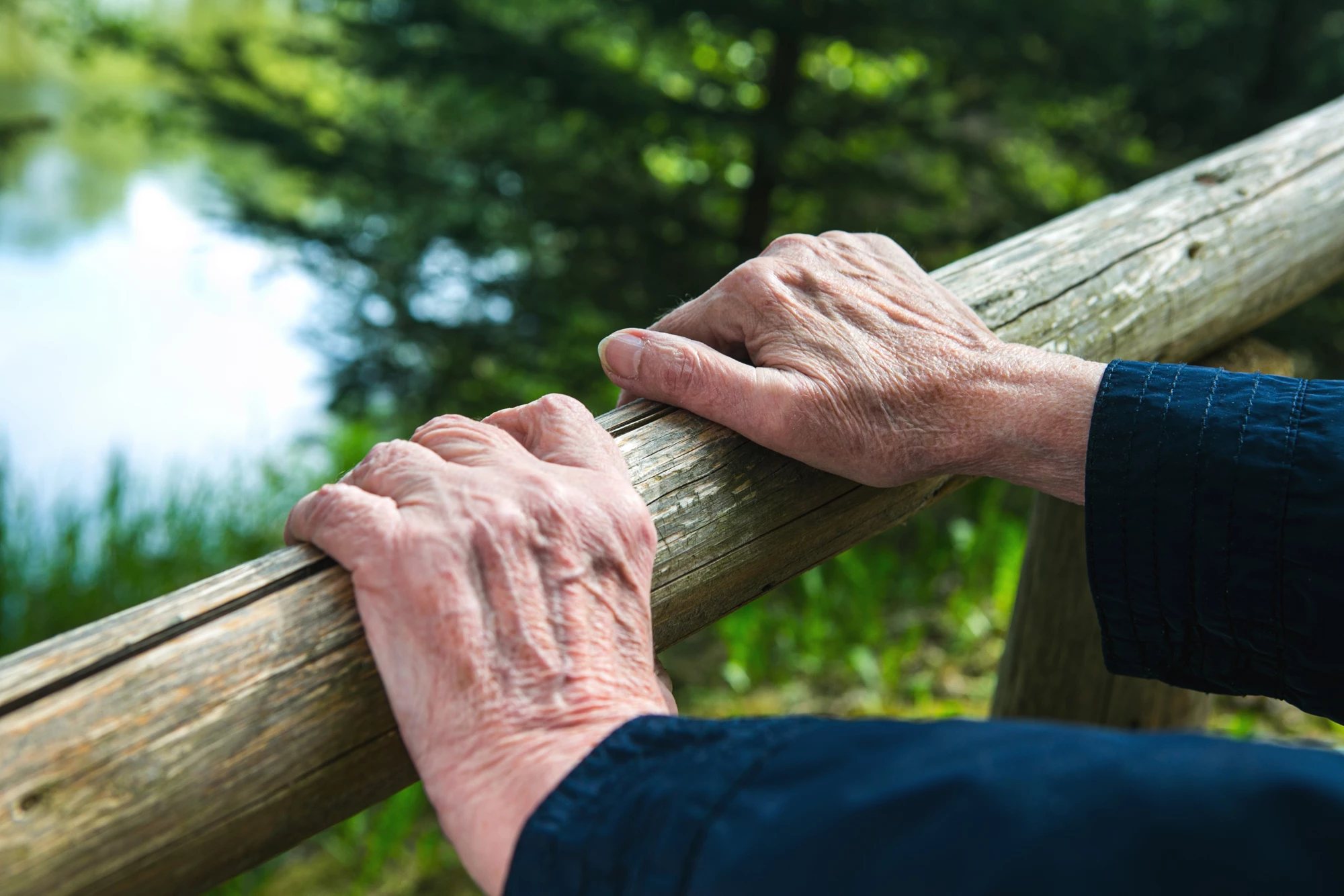 close-up of old womans hands resting at a railing in nature