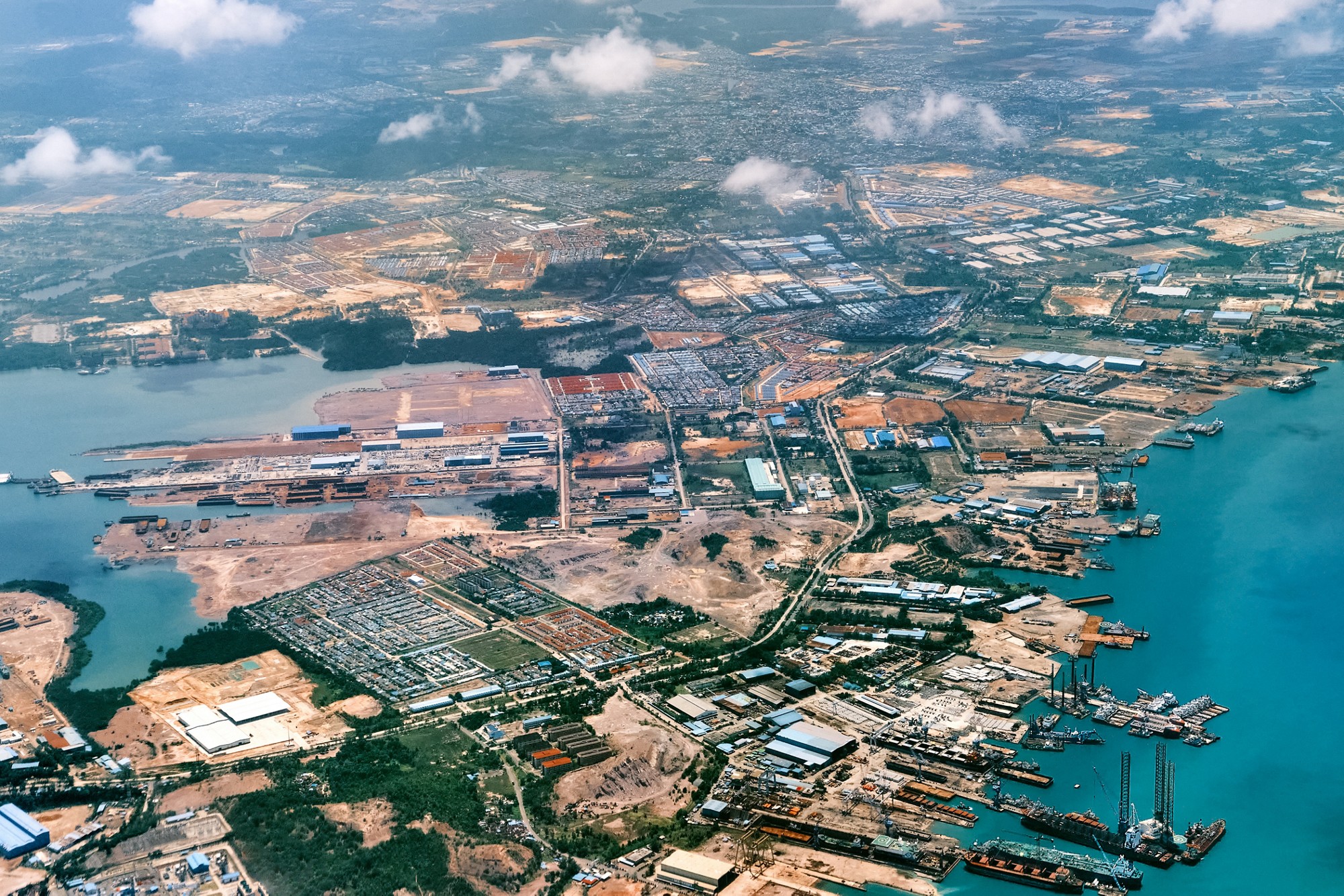 Aerial view of residential, construction or port areas in Strait of Malacca, on airplane route to Malaysia or Singapore. Airplane shot of Malacca Strait coast. Cargo ships, port facilities, warehouses, ship terminals, refineries, residential areas. 