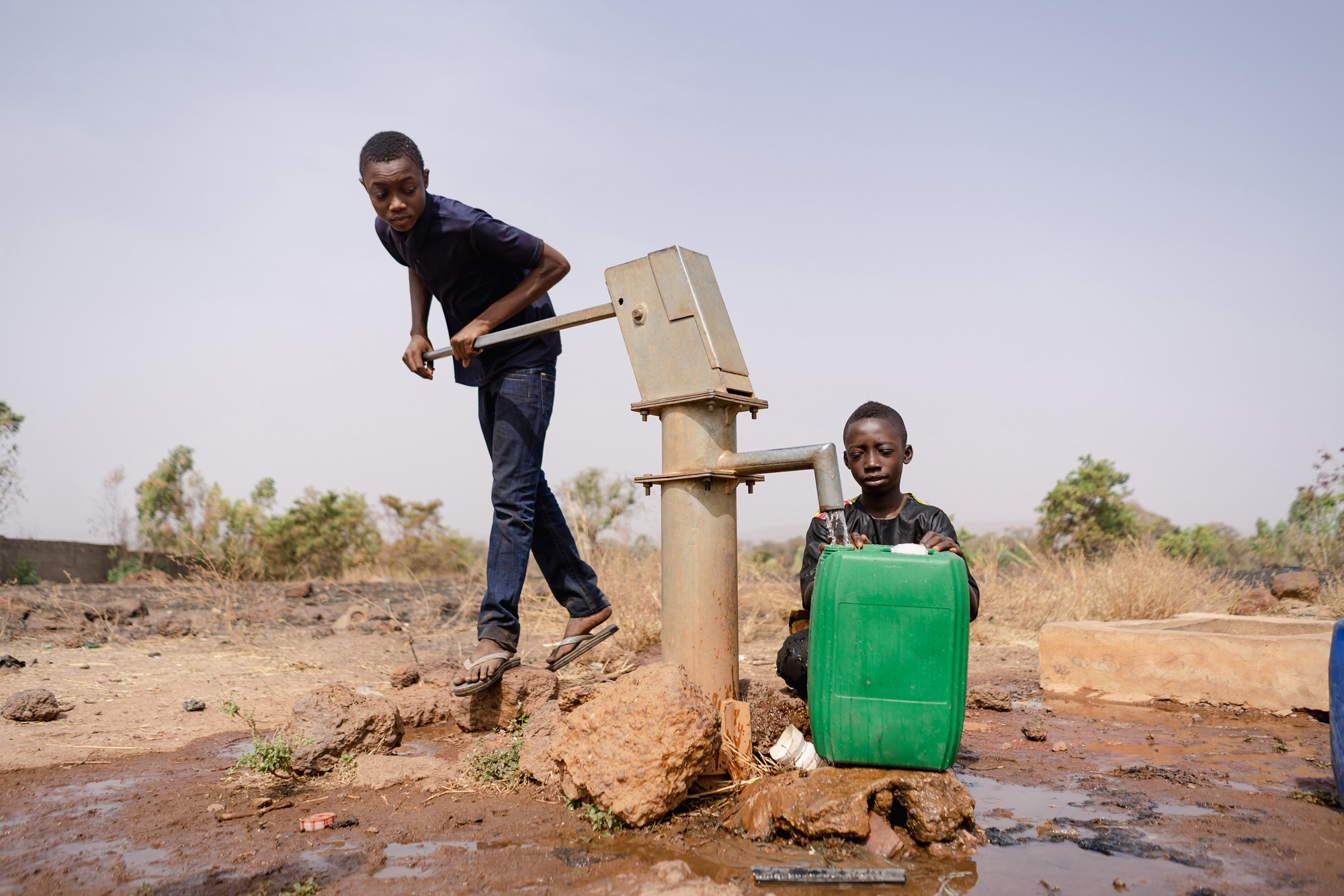 Two African boys busy filling water containers at a remote village pump; water scarcity in developing countries concept
