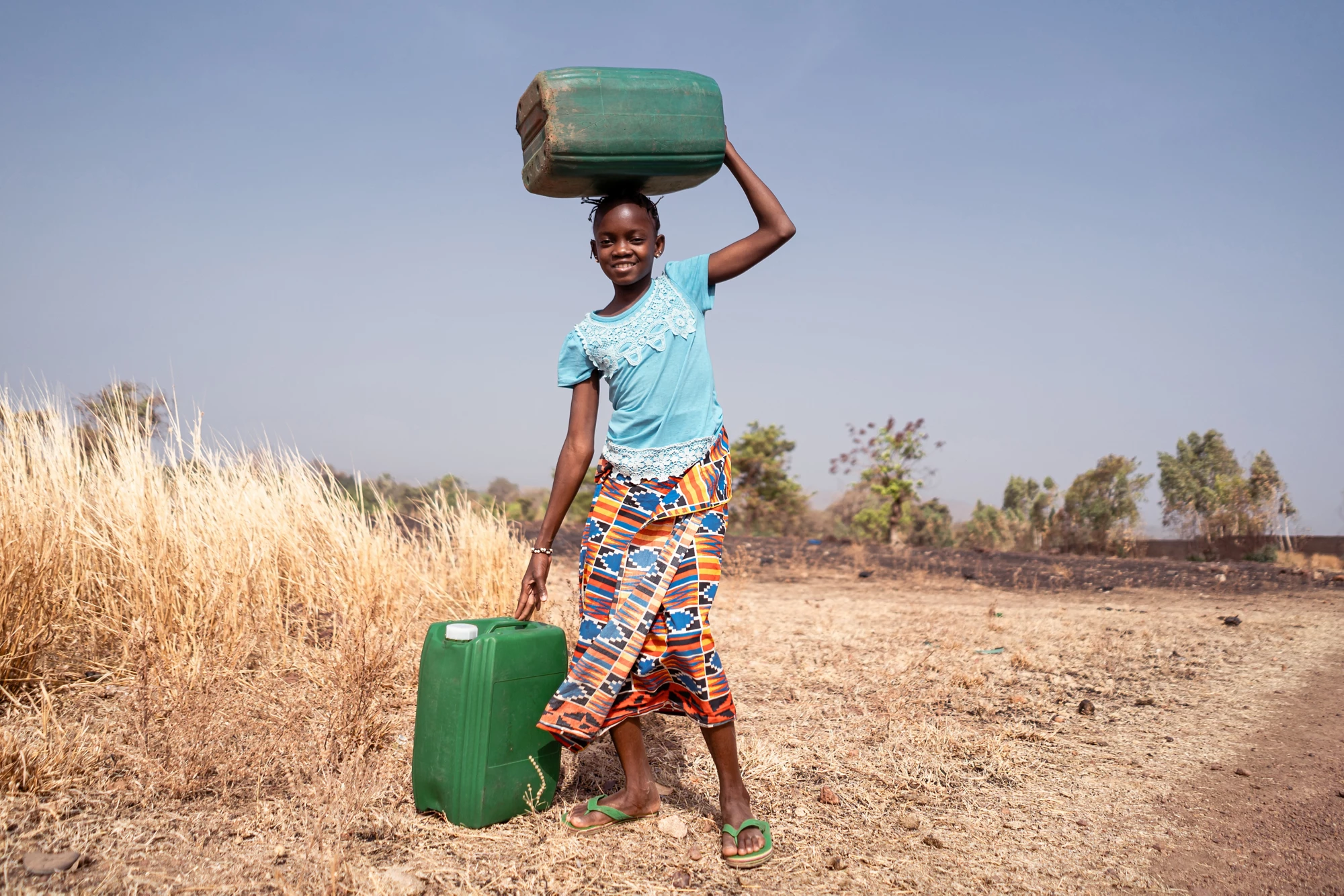 Cute little West African girl with water containers; symbol for the lack of water infrastructure in many poor African villages