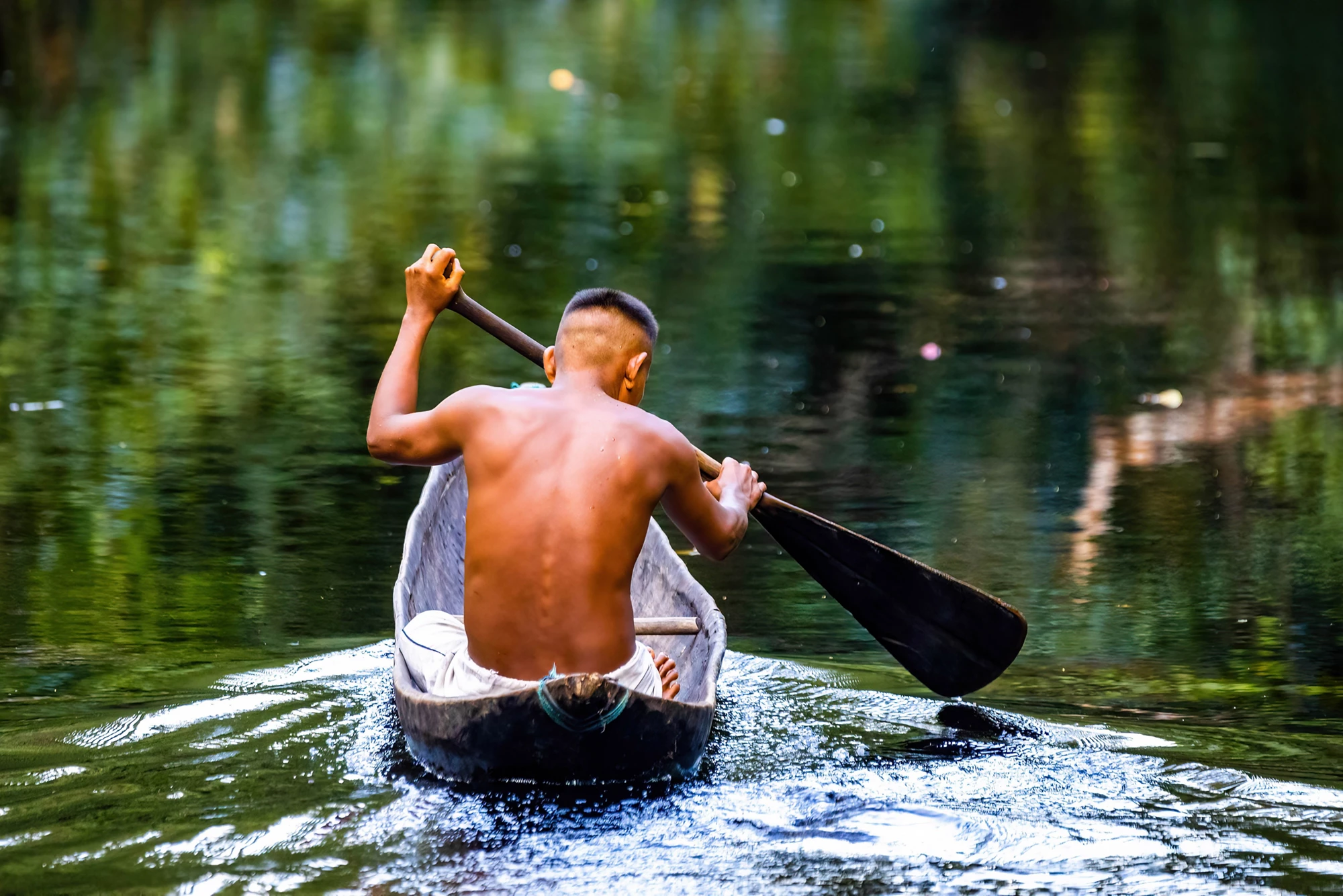 Native tribal man swimming in amazonia rainforest in handmade boat