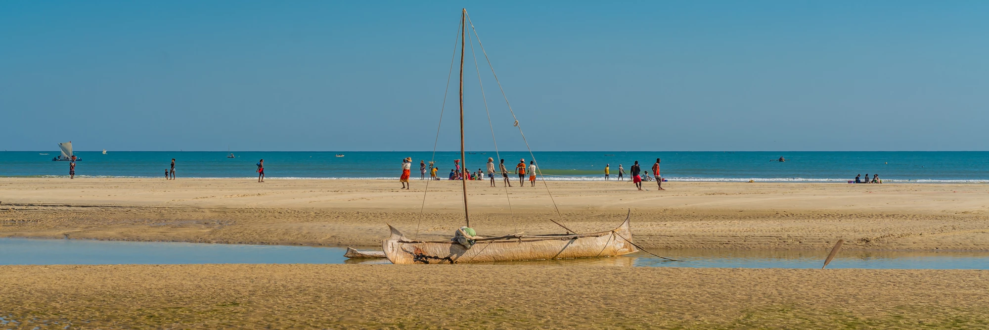 Coastline from Morondava with a baobab wood boat at low tide on sand, background with people panorama