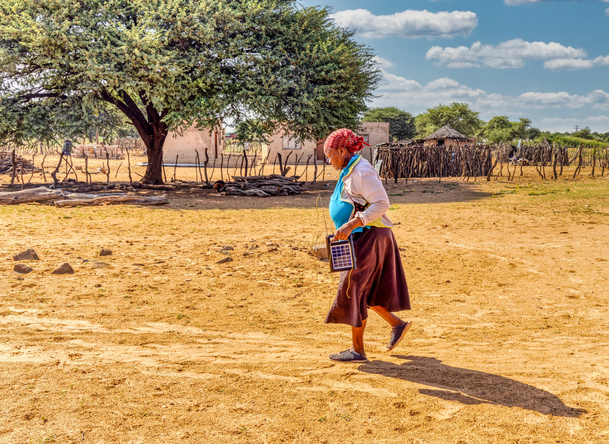 village old african woman using a solar panel with radio, to recharge phones and light, donated by a charity NGO, to improve life in rural areas