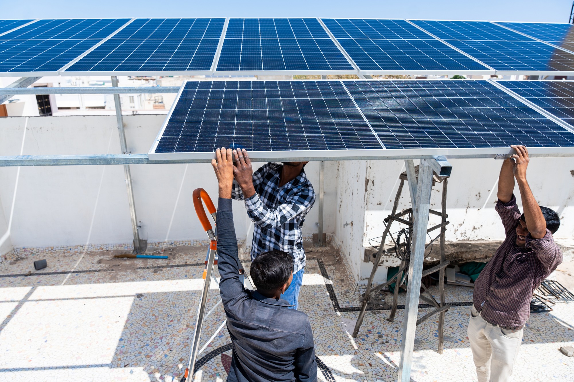 Indian workers installing solar panels on roof of house. Maintenance of photovoltaic panel system. Concept of alternative, renewable energy.