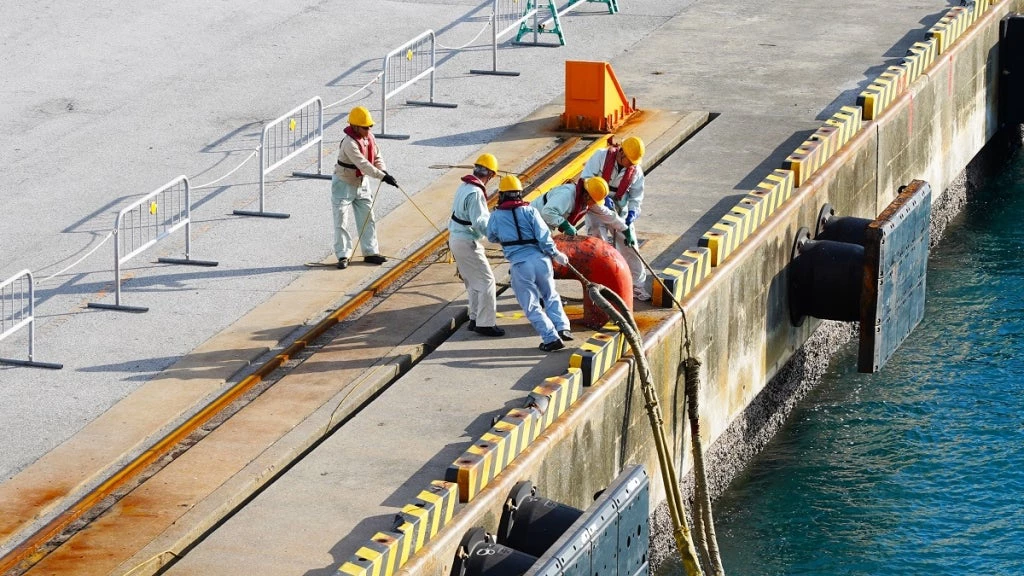 A group of port workers fasten ship mooring ropes to a bollard. Photo: Artem/Adobe Stock