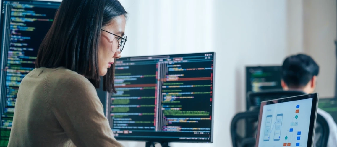 Asian software developers working on multiple screens displaying coding in a modern office