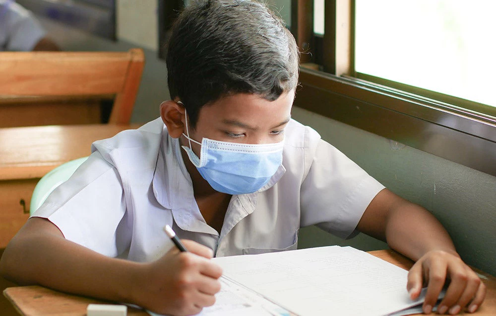 A young boy studies at his desk while wearing a face mask during the COVID-19 pandemic. / Shutterstock