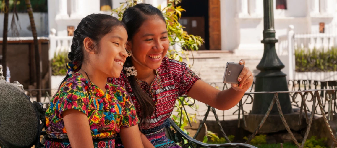 Happy indigenous girls taking selfies with smartphones in a park in Guatemala