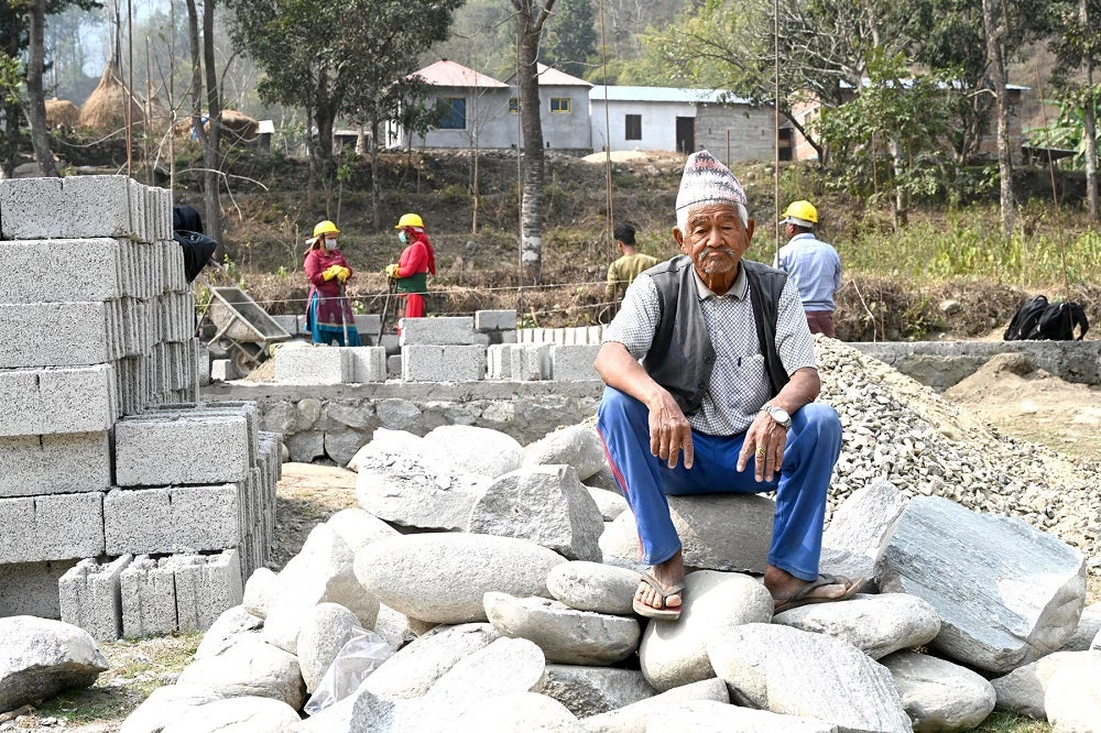 An old man sits upon stones in a construction site