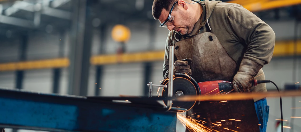 Factory worker cutting metal with a grinder