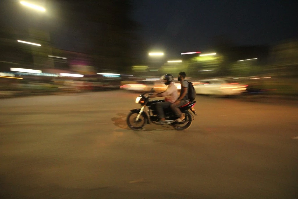 Two young men ride a motorcycle at night.