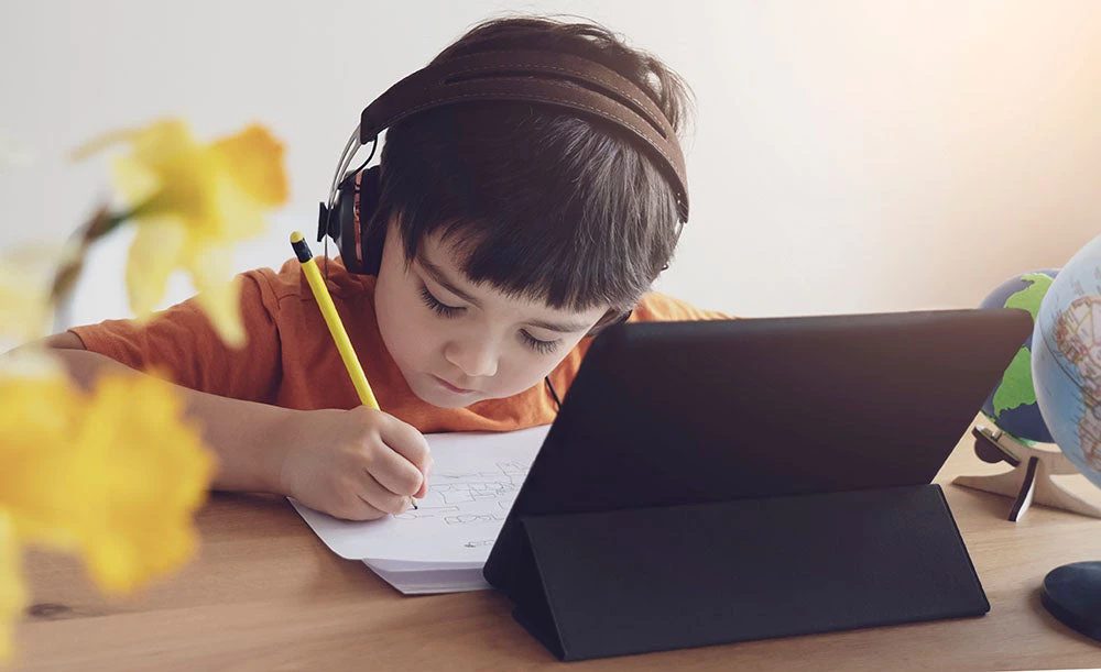 Um garoto em casa estudando com seus fones de ouvido.