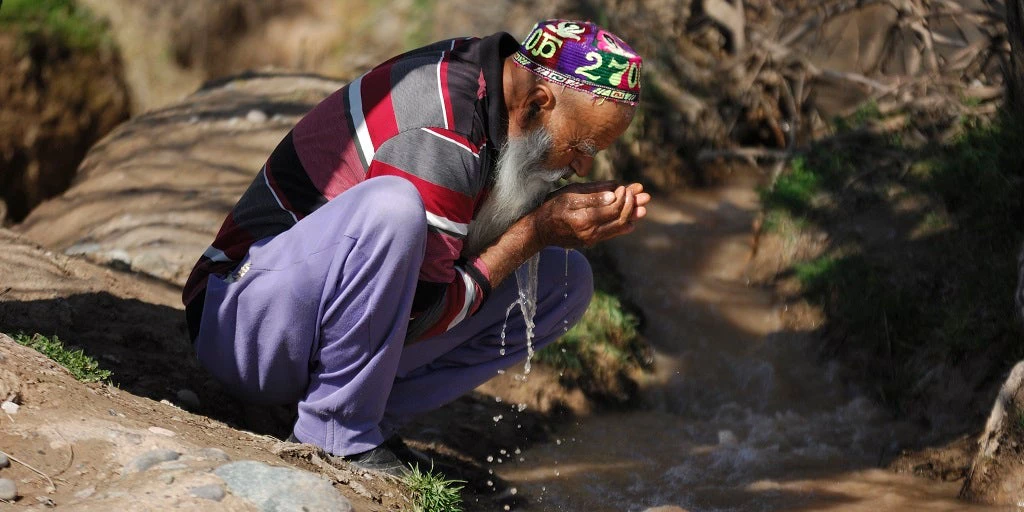 Tajik man drinking water from a stream