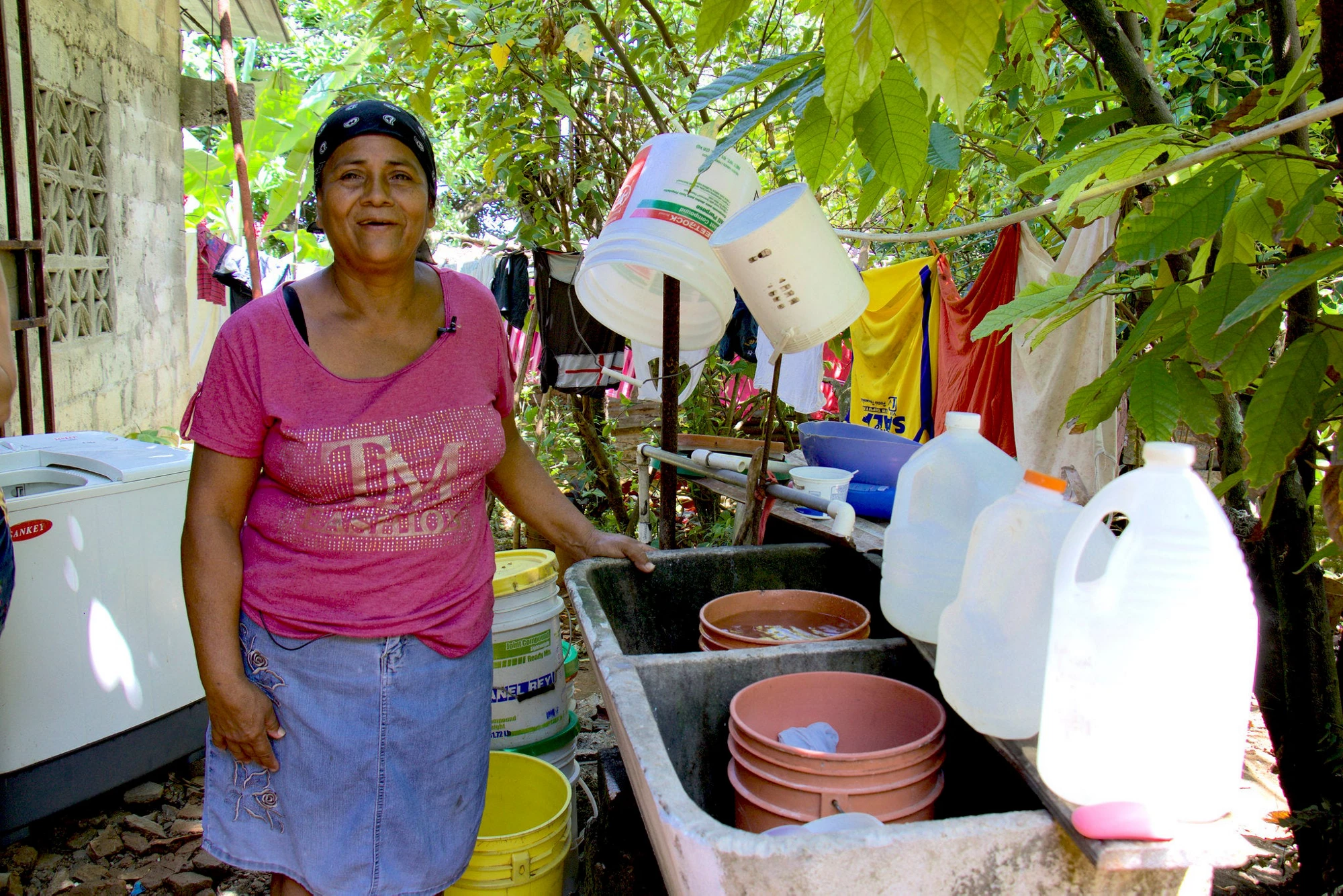 Beneficiaria del proyecto Metro Agua en Colón, Panamá, rodeada de recipientes de agua. 