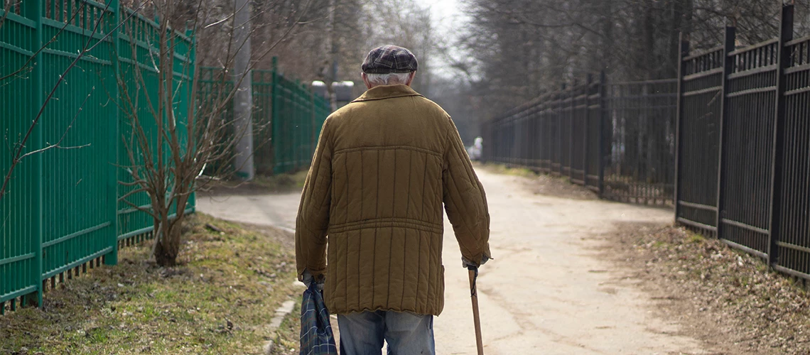 An elderly man with a stick is walking down the street.