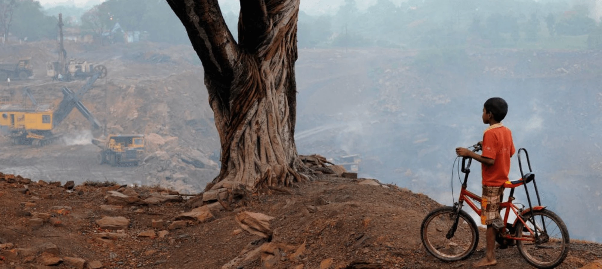 boy rides bicycle next to an open coal mine burning