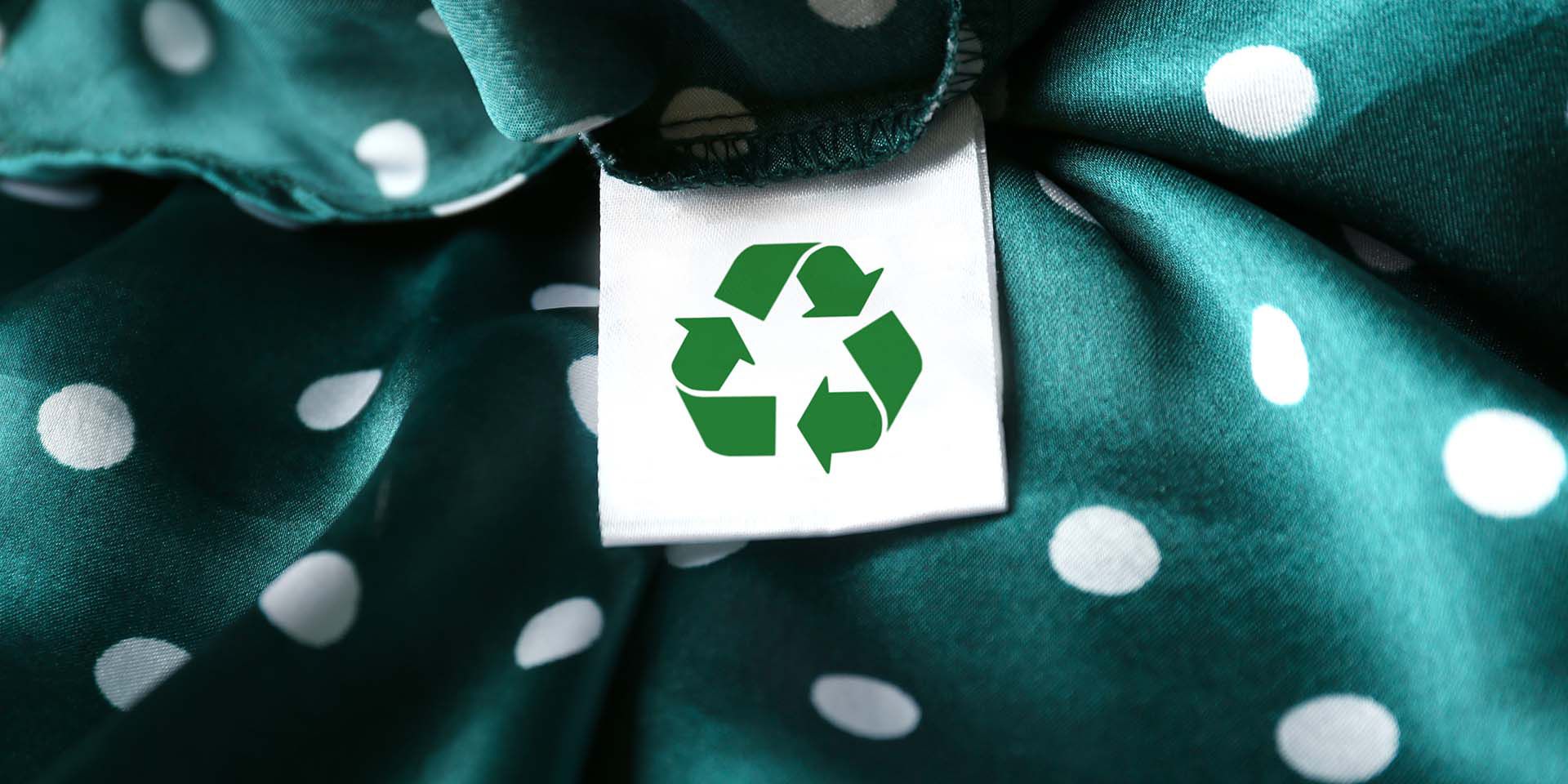 Clothing label with recycling symbol on green garment, closeup
