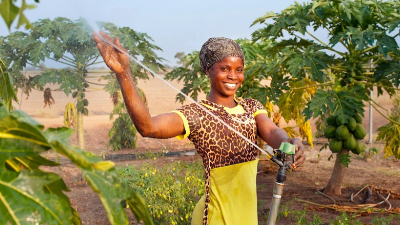 A smiling woman displays her sprinkler irrigation system in Ghana.