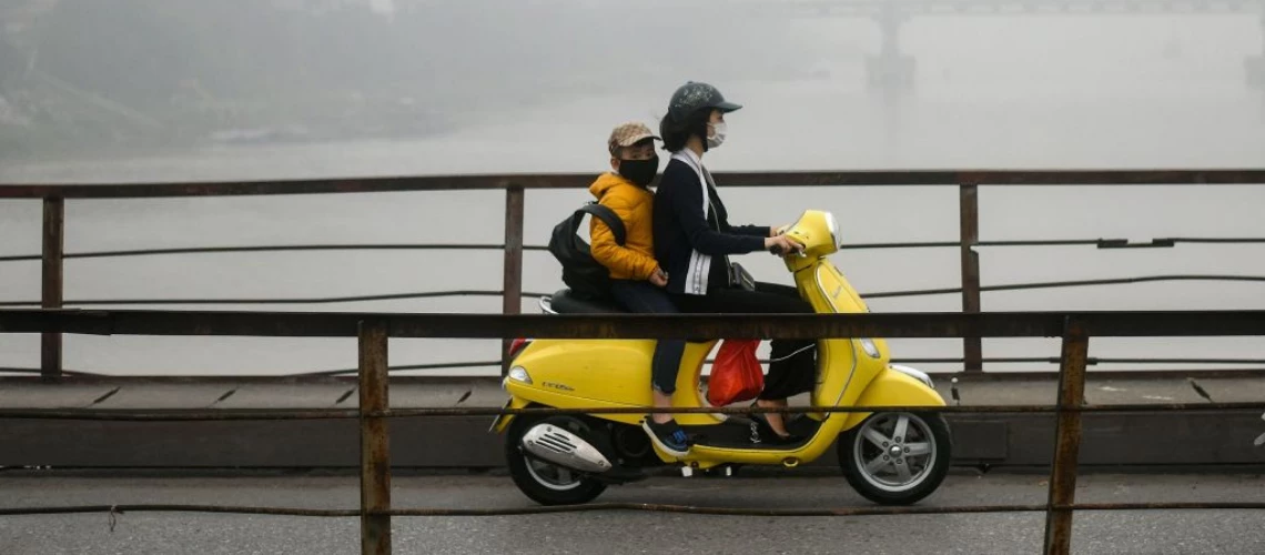 A Vietnamese woman wearing a face mask rides on a bridge amidst a blanket of smog over Hanoi. 