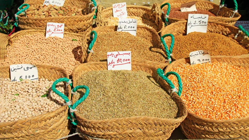 Diferentes tipos de grano en un mercado, con carteles identificativos y el precio en árabe.