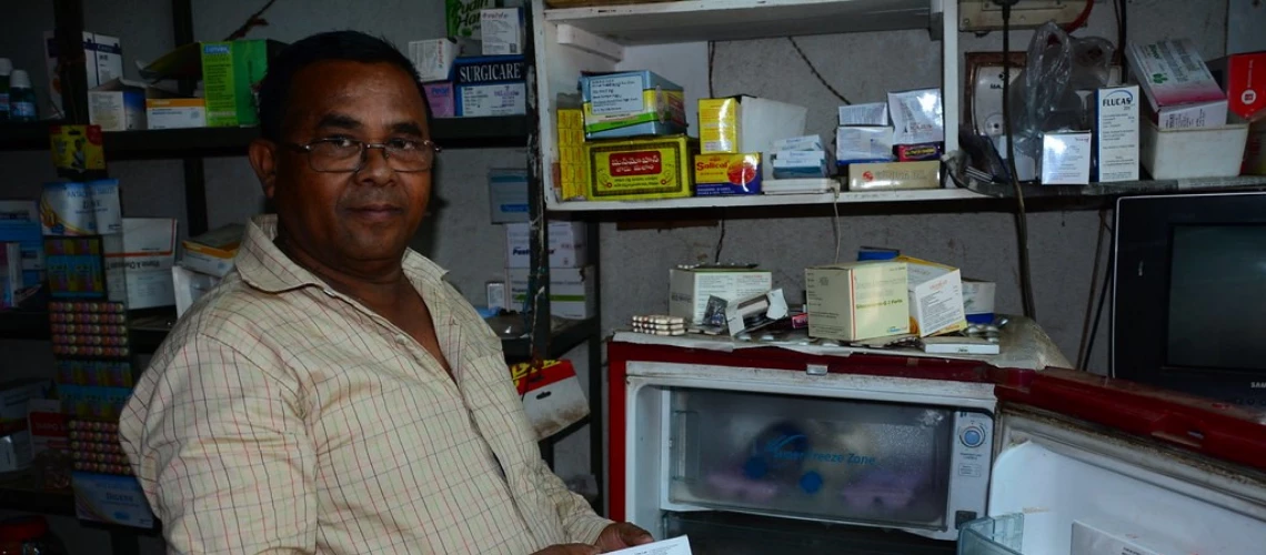 Bespectacled man holding a box of medicine in a pharmacy