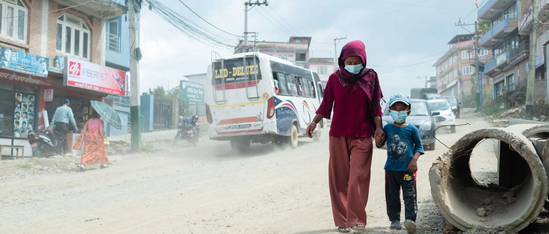A woman and a child hold hands and walk on a dusty road in Nepal