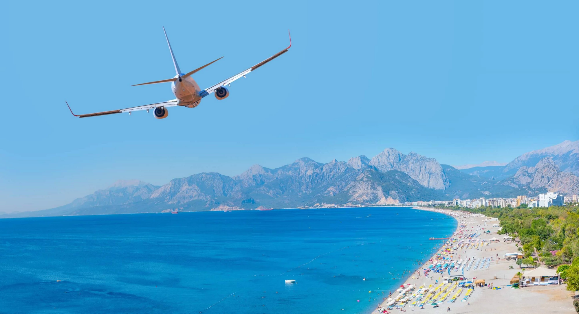 A white airplane flies over the konyaalti beach and blue sea in Antalya Turkey