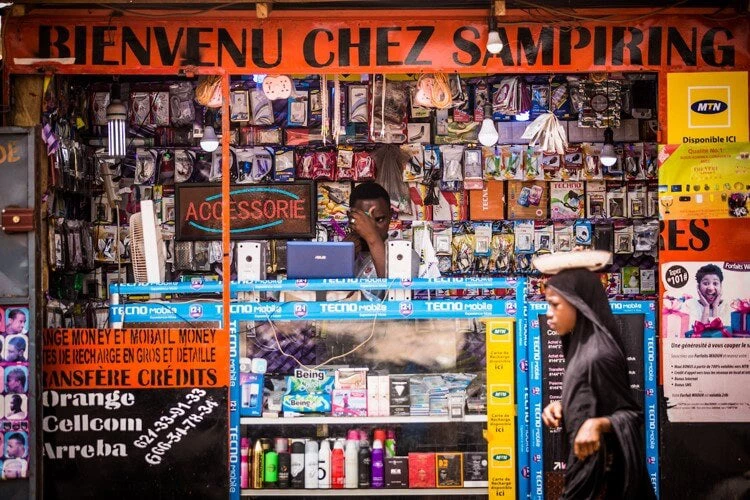 A seller in Koba Guinea checks his phone while waiting for customers in his shop along the road