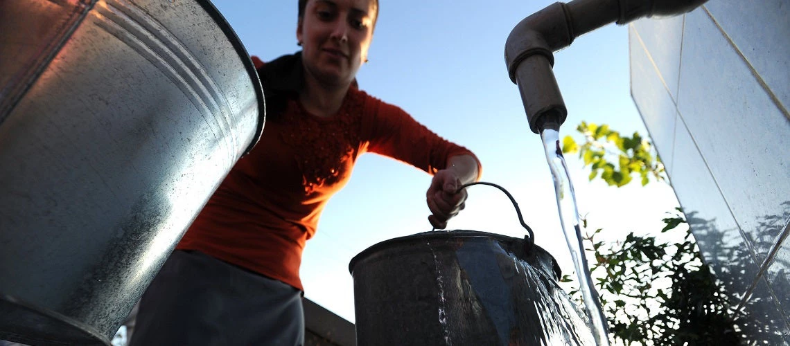 Women filling up two metal buckets of water with an open faucet. 