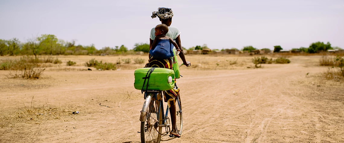 Barry Aliman, 24 years old, rides her bicycle with her baby to collect water for her family, Sorobouly village near Boromo, Burkina Faso. For many women, regular childcare facilities are not an option for many women, given transportation difficulties and  limited time available. © Ollivier Girard, CIFOR  