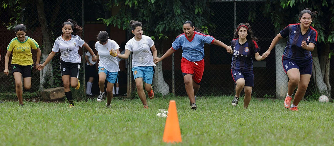 Niñas corriendo juntas tomadas de la mano en el campo de fútbol de una escuela en El Salvador 