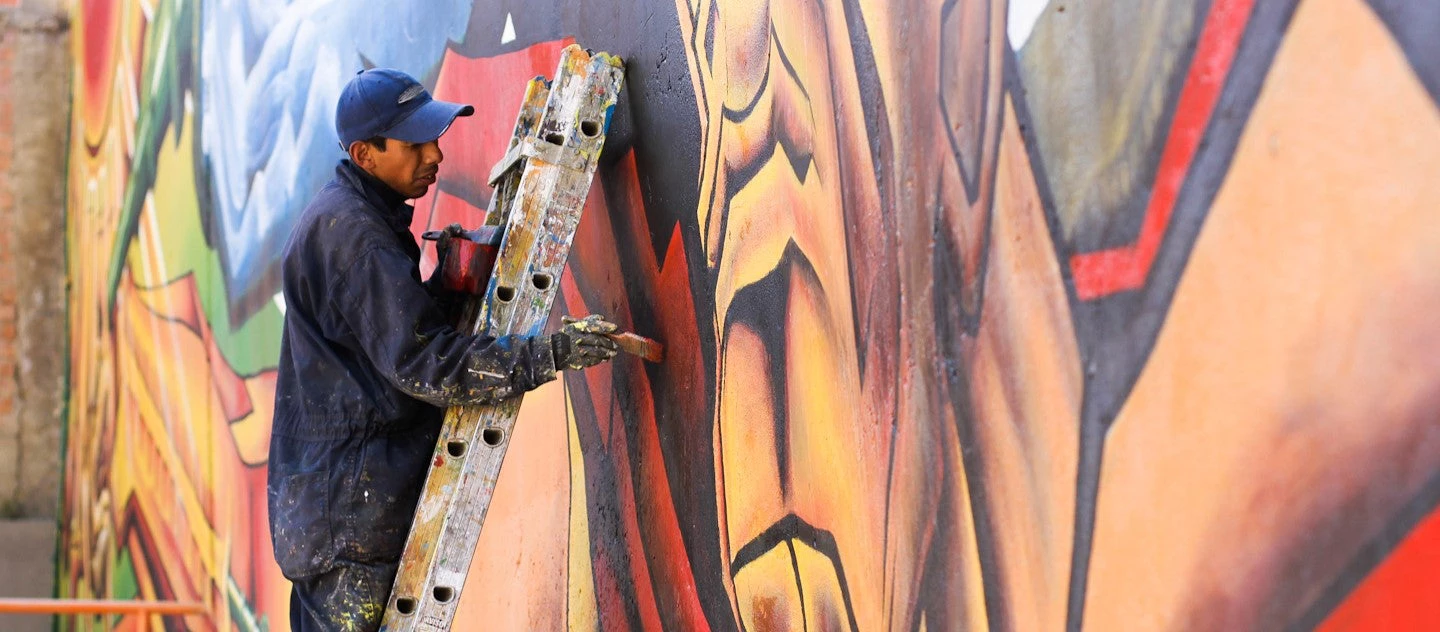 Pintor trabajando en un mural multicolor en la periferia urbana de La Paz, Bolivia. 