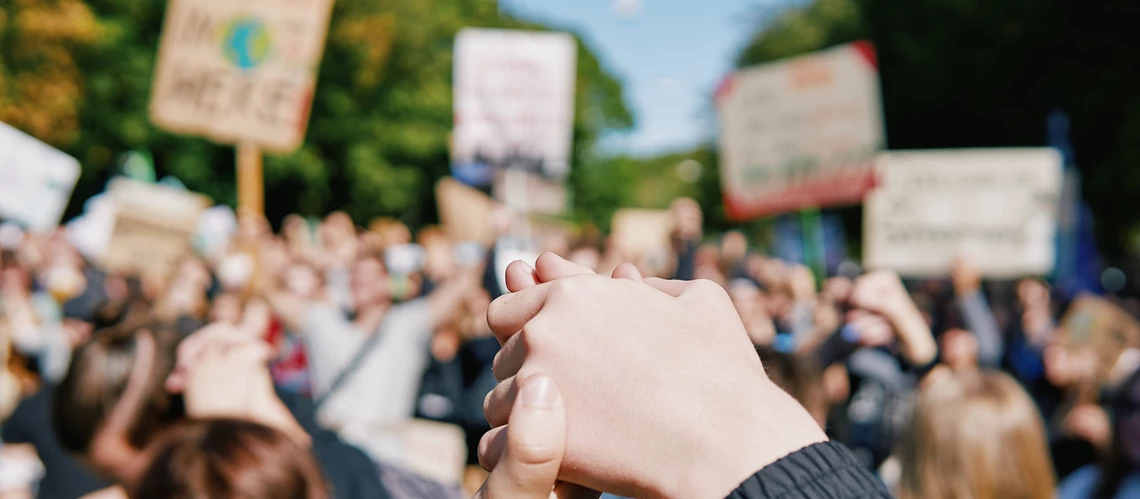 Hands joining at a climate march, in front of a crowd carrying signs with shallow depth of field.