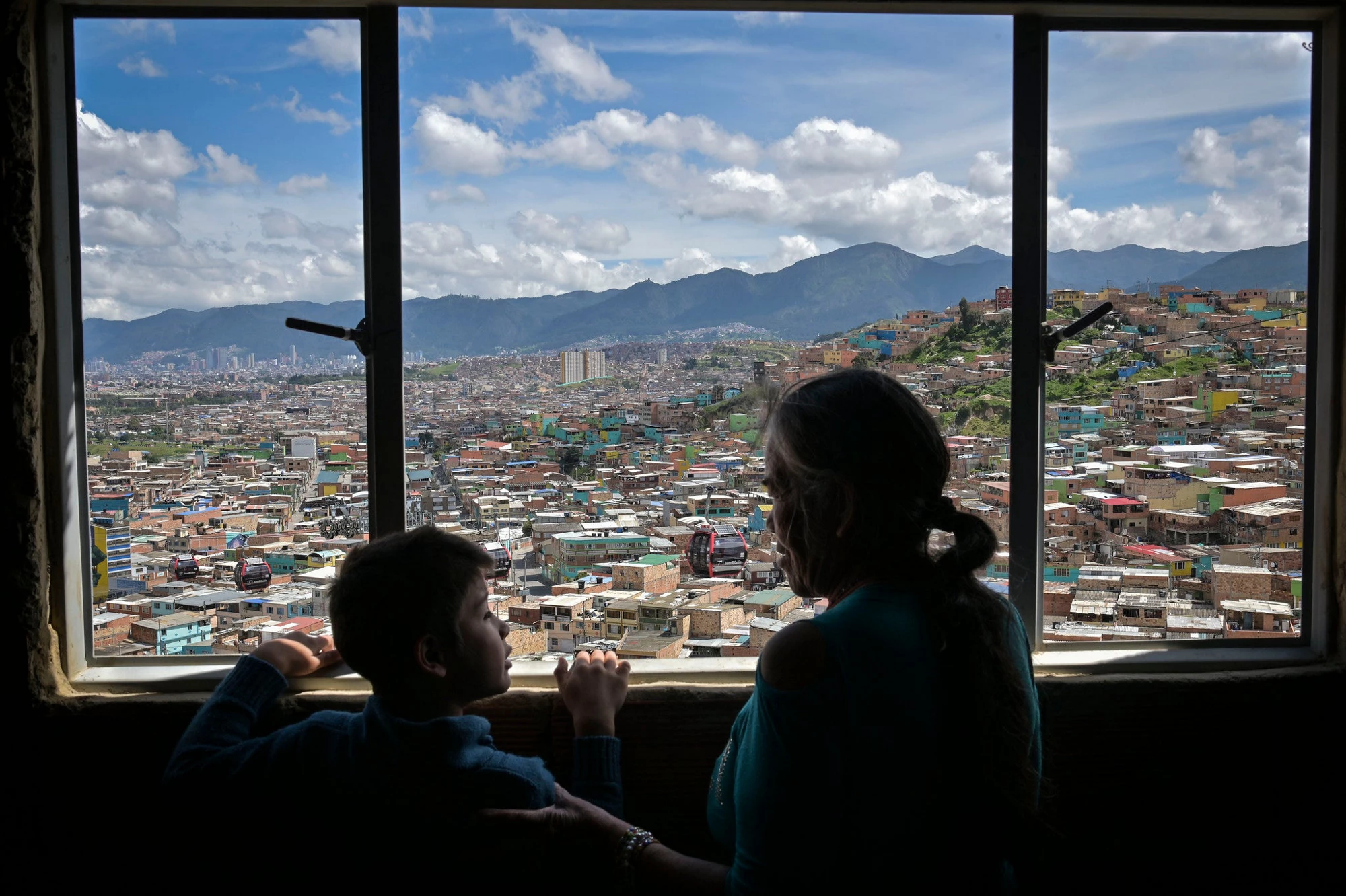 A grandmother and grandson look out the window of their home in Colombia
