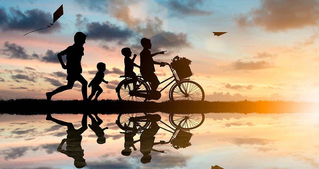 Des enfants à vélo et poursuivant des avions en papier et des cerfs-volants au coucher du soleil