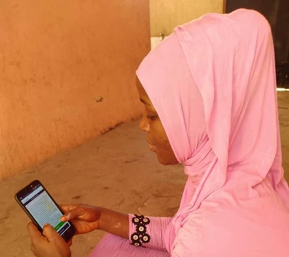 A young woman wearing a pink hijab in Bamako is learning about solid waste before validating its presence on an aerial image.