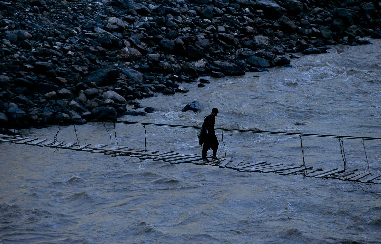 Man crossing rope bridge over river in Pakistan