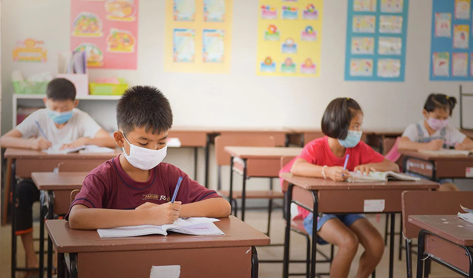 Niño sentado en su escritorio con su máscara. / Shutterstock