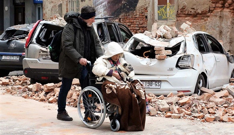 Citizens pass by cars destroyed in the quake