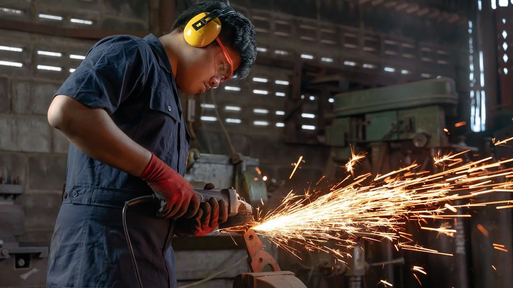 Engineer operating angle grinder hand tools in manufacturing factory.