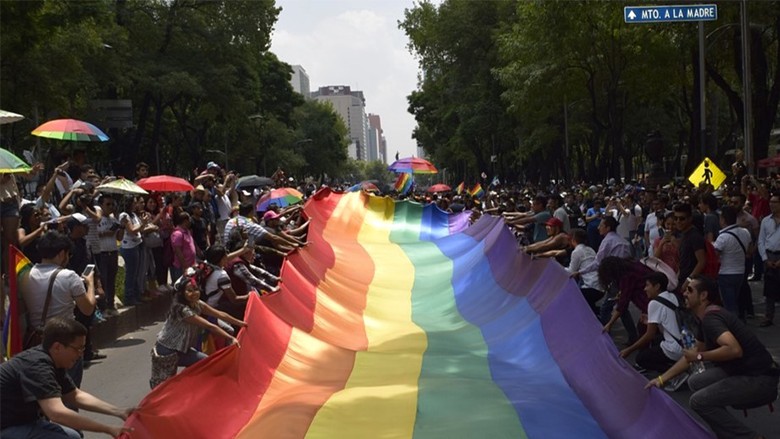 People holding a large rainbow flag during a Pride Parade in Mexico. Image by Gabriela Serralde from Pixabay.