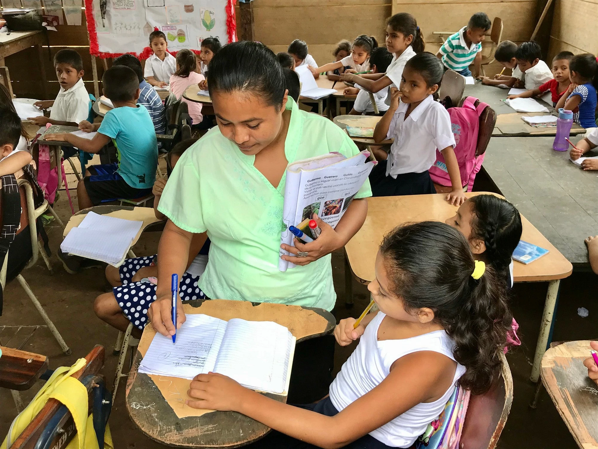 Maestra corrige la tarea de una niña en una escuela rural 