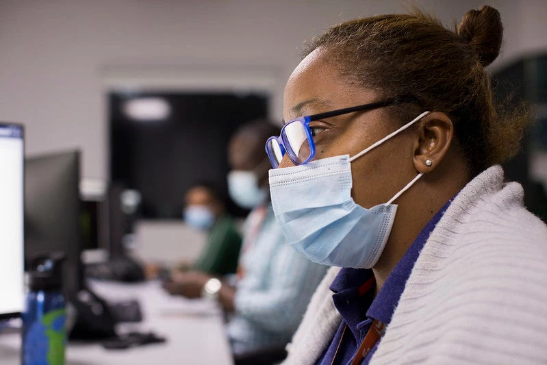 A woman wearing a health mask works in front of a computer