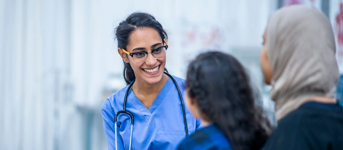 A female doctor smiles at a woman and her young child.