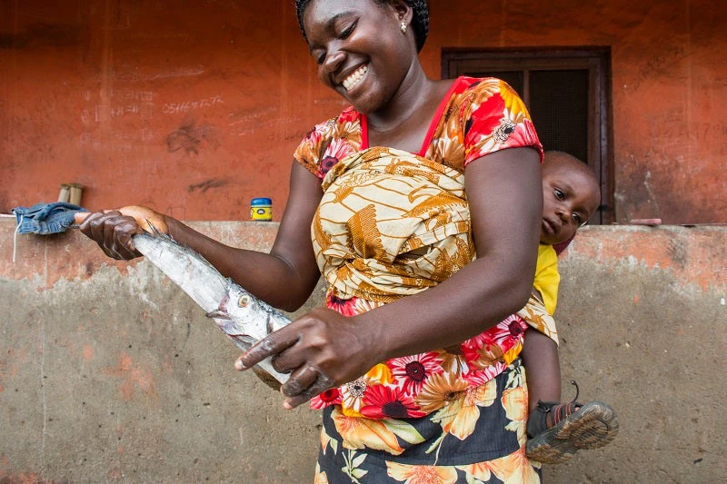 A woman cleans a fish while carrying her child on her back in Ghana. © Andrea Borgarello / World Bank