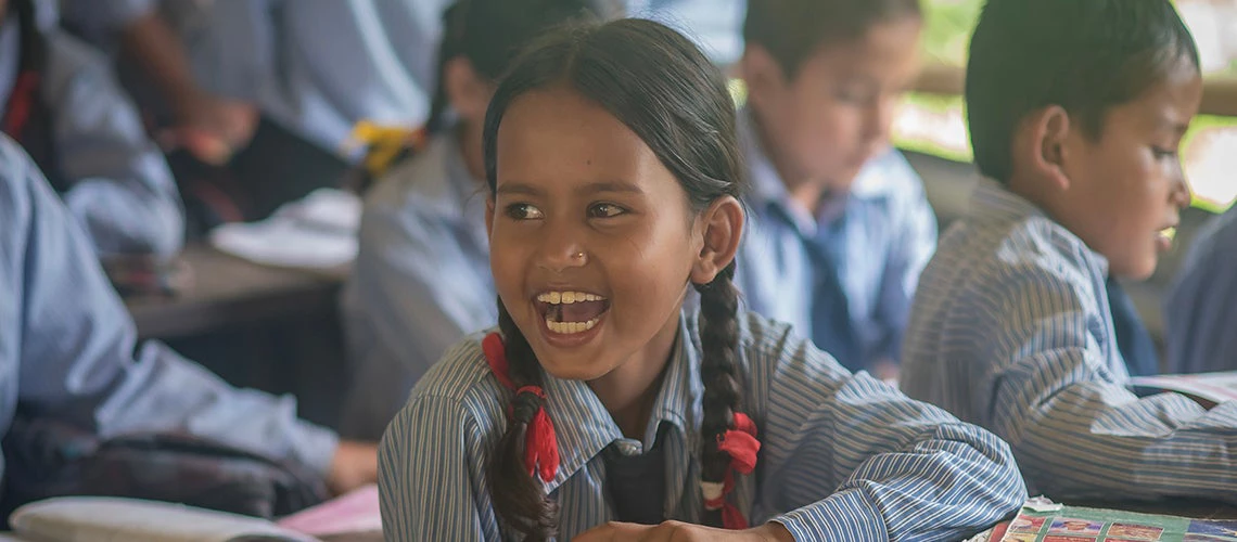 Girl from a village in the mountains of Nepal is attending school and laughing in the classroom.
