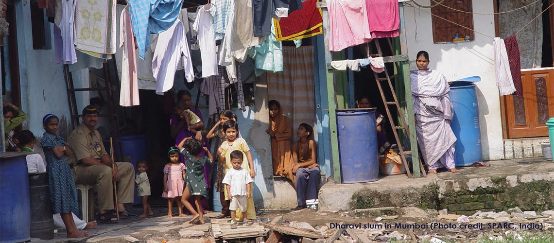 Slums in India with adults and kids sitting by colorful clothes hanging to dry.