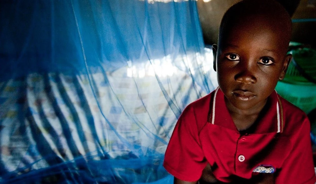 A young boy sits in front of a protective malaria bed net. South Sudan.
