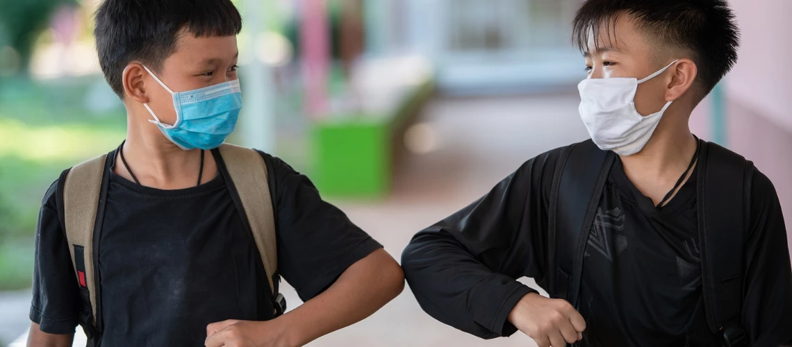 Two Asian boys wearing masks fist bump. Photo: Sutipond Somnam / Shutterstock
